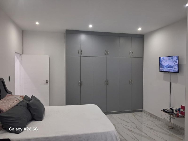 A modern bedroom featuring sleek grey built-in cupboards, polished marble-look tiled flooring, and recessed ceiling lighting.