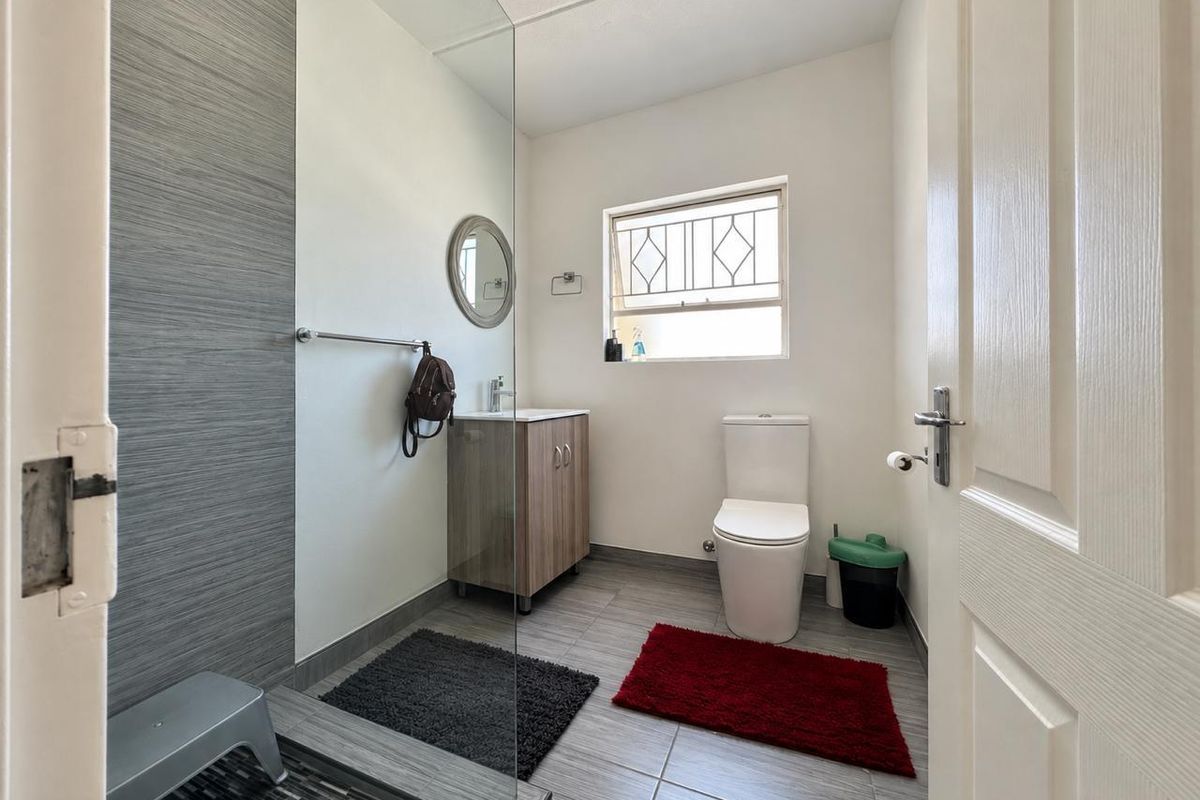 A modern bathroom featuring a glass-enclosed shower, vanity cabinet with basin, and a toilet, finished with neutral grey floor and wall tiling.