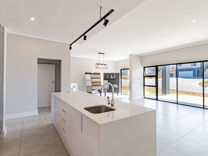 Modern open-plan living area featuring a central kitchen island with sink, sleek tiled flooring, and large sliding glass doors providing ample natural light.