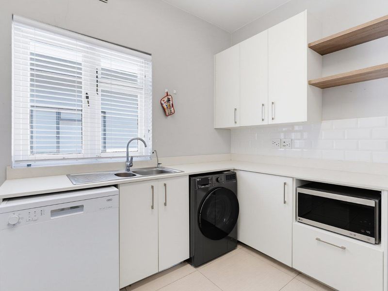 A clean, modern kitchen featuring white cabinetry, subway tile backsplash, stainless steel sink, and integrated shelving, offering a bright and functional workspace.