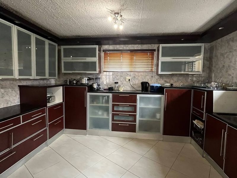 A functional kitchen featuring dark wood-toned cabinetry, tiled flooring, and ample storage space with frosted glass accents, offering a classic layout.