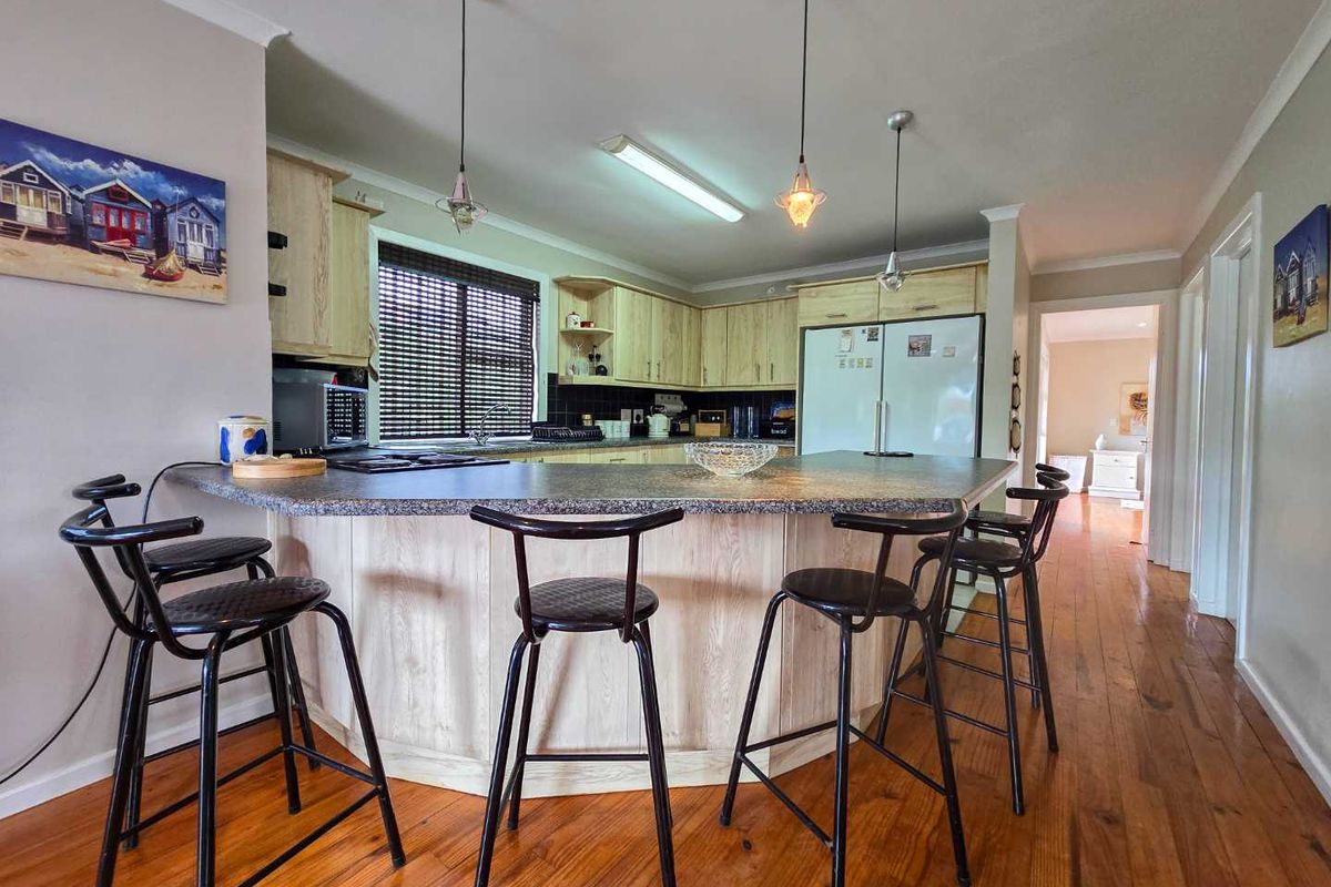 A functional kitchen featuring light wood cabinetry, a large breakfast bar with granite-style countertops, and hardwood flooring throughout the space.