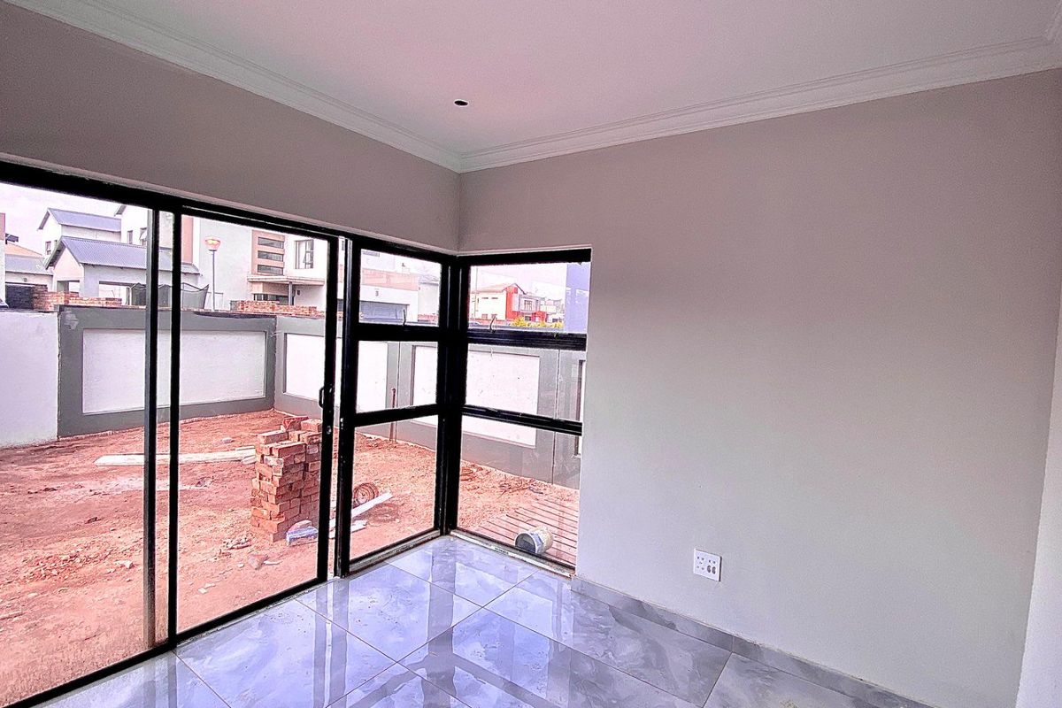 A bright, empty living area featuring large sliding glass doors that open onto an unfinished backyard space with tiled flooring and neutral walls.