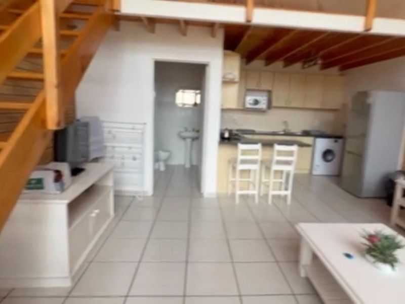 Open plan living area featuring a wooden staircase to a mezzanine level, tiled flooring, and an integrated kitchen with adjacent bathroom access.