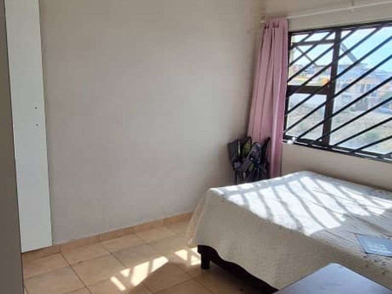 A bedroom featuring tiled flooring, a built-in wardrobe, and a window with security bars. Visible water staining on the wall requires attention.
