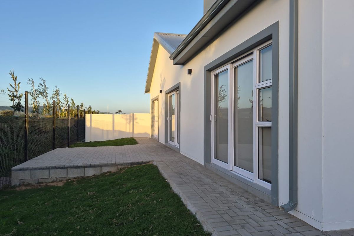 Rear view of the property featuring a paved patio area, manicured lawn, and modern sliding glass doors leading into the home.