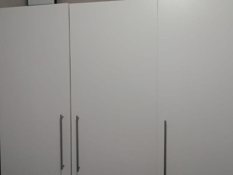 A bedroom featuring a modern, white built-in wardrobe with sleek metal handles.