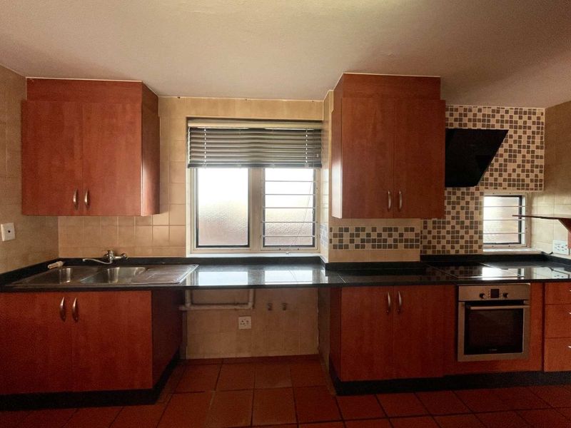 A functional kitchen featuring dark granite countertops, wood-finish cabinetry, built-in oven, extractor fan, and tiled flooring with a neutral backsplash.