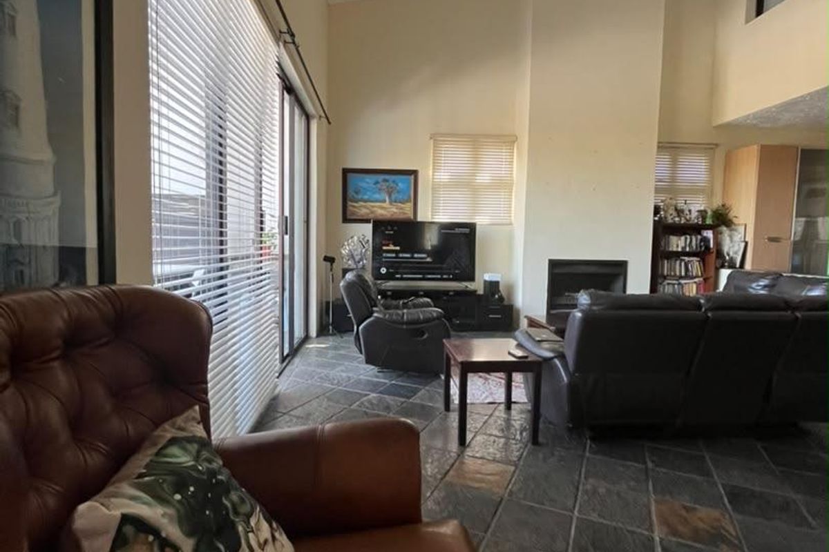 Spacious living room featuring vaulted ceilings, slate tile flooring, and a built-in fireplace, with large sliding doors providing access to the exterior.