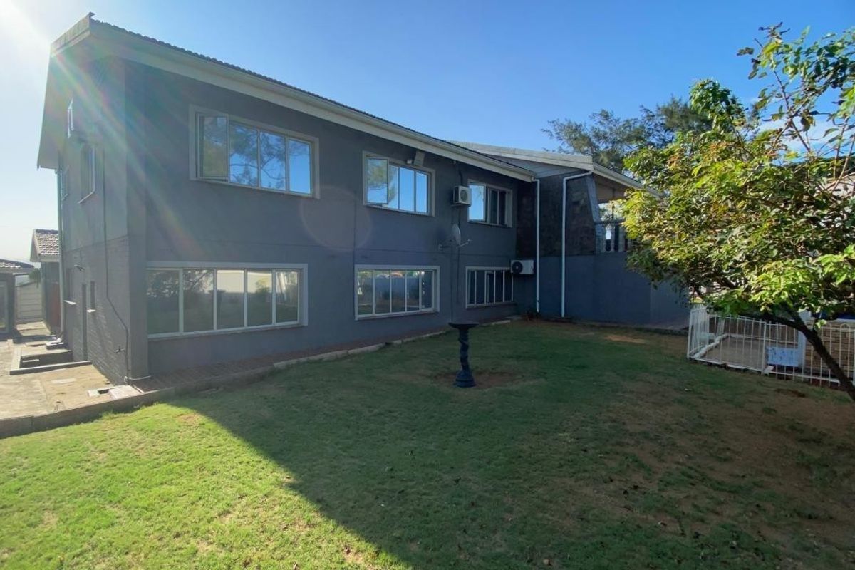 Rear view of the property featuring a spacious lawn, paved patio area, and modern grey exterior walls with aluminium window frames.