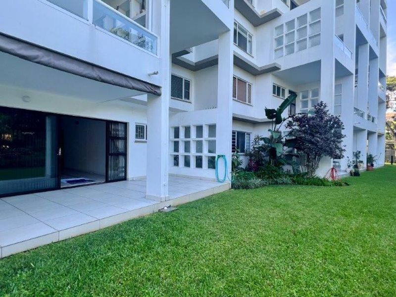 A ground floor apartment featuring a tiled patio with a retractable awning, providing direct access to a well-maintained communal garden area.