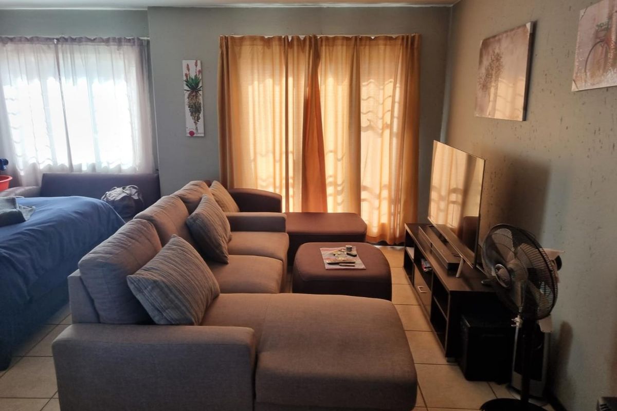 A living room area featuring tiled flooring and a sliding glass door leading to an outdoor space, with visible wall surface wear.