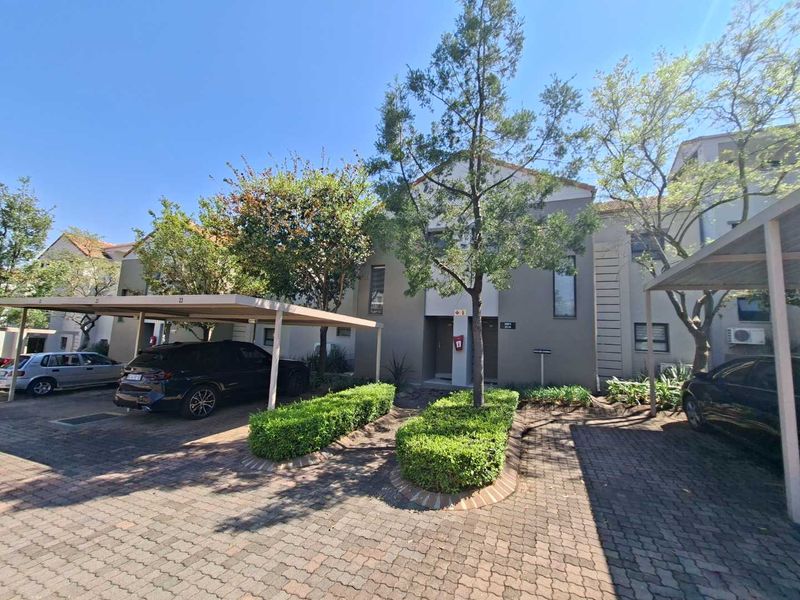 Front exterior view of the apartment complex featuring covered parking bays, paved driveway, and well-maintained landscaped garden areas.