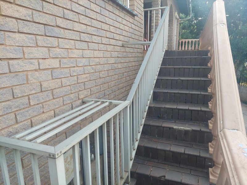 Exterior brick staircase leading to the entrance, featuring a metal handrail and decorative balustrade, showing signs of wear and weathering.