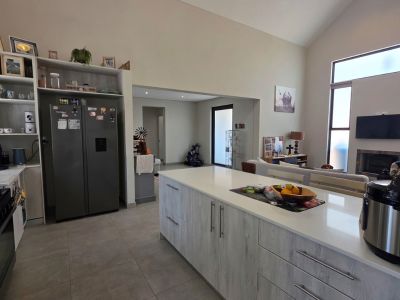 Spacious open-plan living area featuring a modern kitchen with a large island, quartz countertops, tiled floors, and a cozy fireplace under a vaulted ceiling.