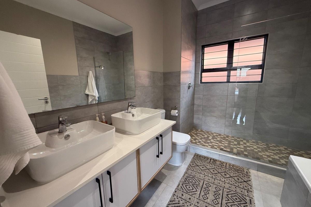 Modern bathroom featuring a double vanity with vessel sinks, large wall mirror, and a spacious walk-in shower with mosaic tile flooring.