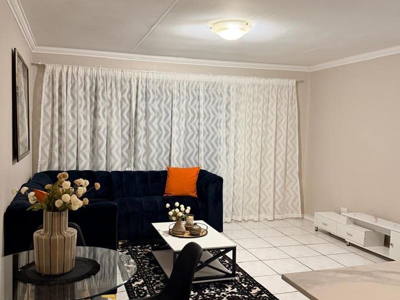 An open-plan living and dining area featuring neutral tiled flooring, clean wall finishes, and a bright, functional layout.