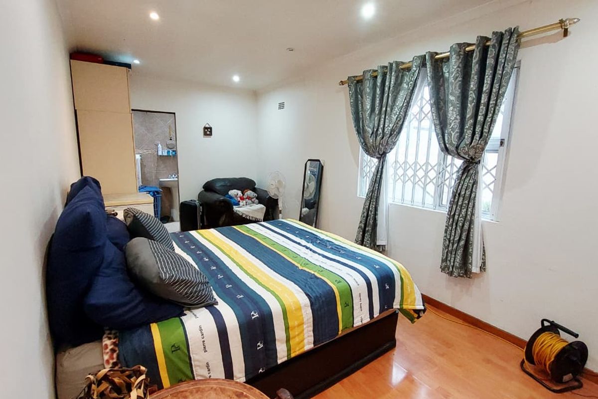A bedroom featuring laminate flooring, recessed ceiling lighting, and a window fitted with security bars and decorative curtains.