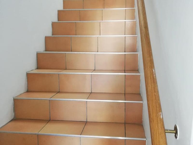 A functional staircase featuring terracotta-style floor tiles and a mounted wooden handrail, providing access between office levels.