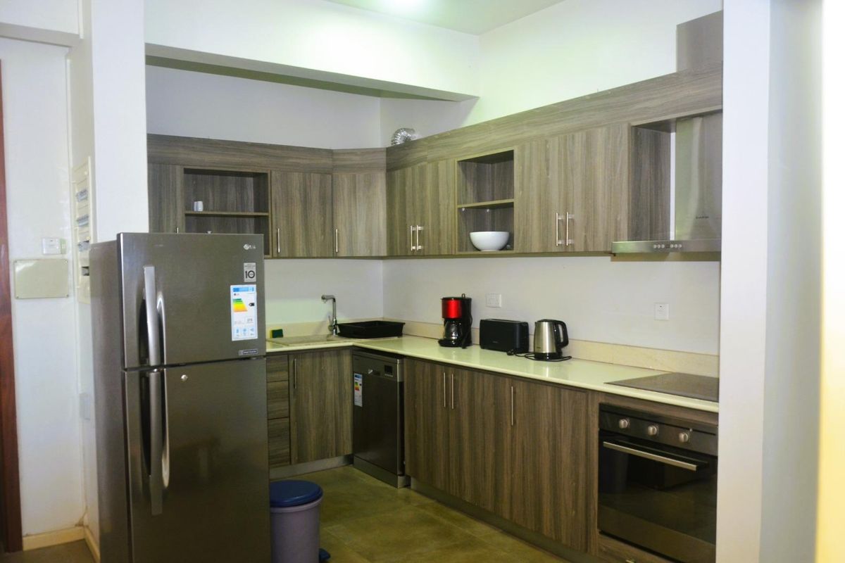 A functional kitchen featuring wood-grain cabinetry, stone countertops, a built-in oven, extractor fan, and integrated dishwasher.