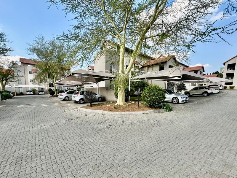 Exterior view of the apartment complex featuring paved parking areas with shade cloth carports and established trees.