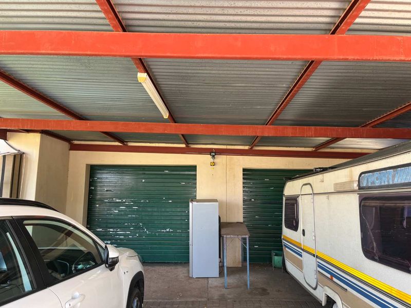 A covered double garage area featuring corrugated metal roofing, steel support beams, and dual roller doors with visible wear.