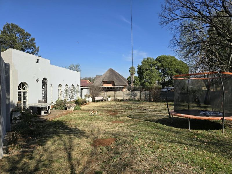 Spacious rear garden featuring a paved patio area, arched architectural details on the house facade, and a secure perimeter wall.
