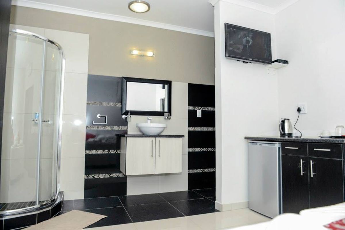 A modern bathroom featuring a glass-enclosed corner shower, a floating vanity with a vessel sink, and a compact kitchenette area with built-in cabinetry.
