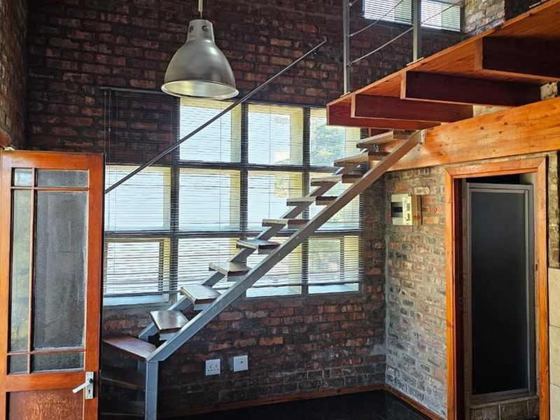 Spacious living area featuring industrial-style exposed brick walls, vaulted ceilings, and a prominent timber staircase leading to a mezzanine level.