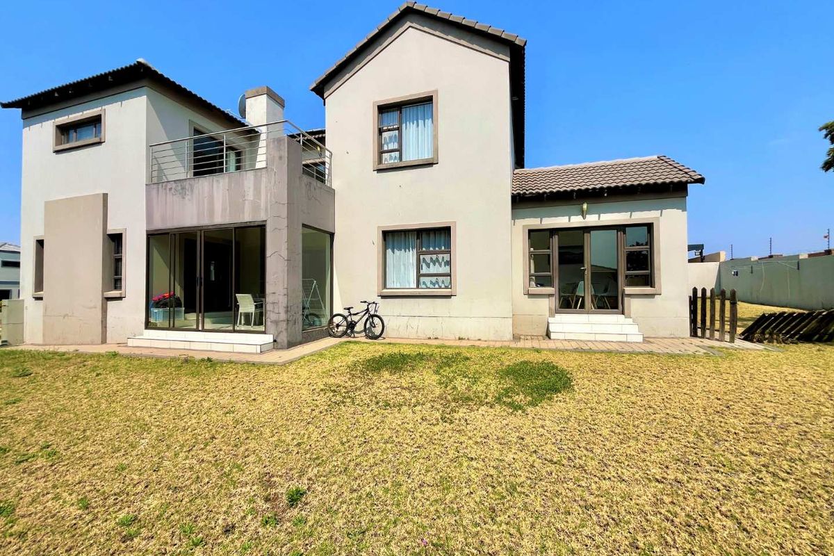 Rear view of a two-story residential property featuring a paved patio, upper-level balcony with metal railing, and a private lawn area.