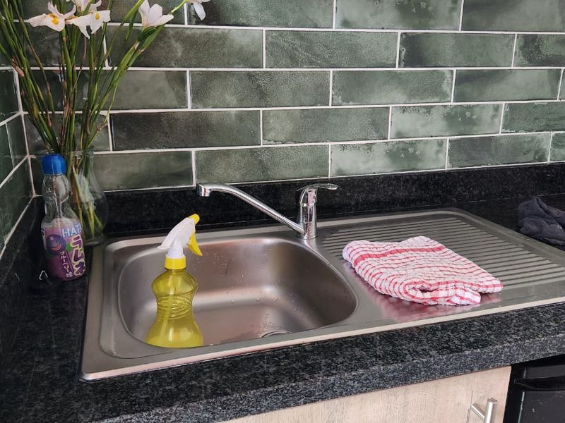 A close-up view of a kitchen sink area featuring a stainless steel basin, modern mixer tap, granite countertop, and stylish green subway tile backsplash.
