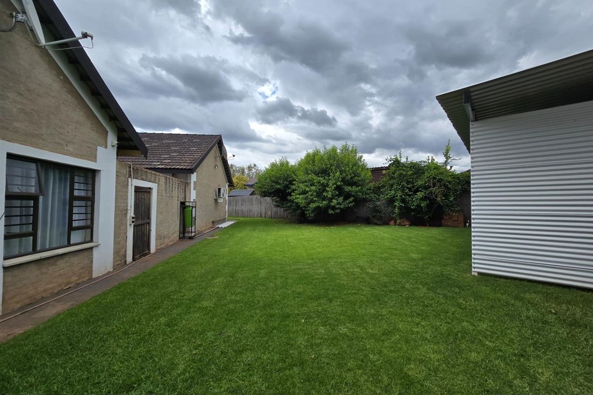 A spacious rear garden area featuring a well-maintained lawn, bordered by the main house structure and a detached corrugated metal outbuilding.