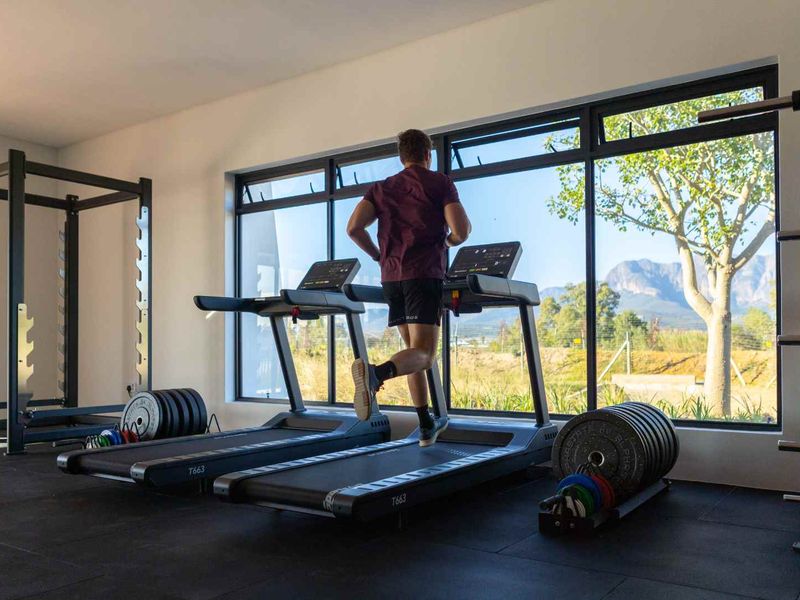 A modern, well-lit home gym featuring large windows with scenic mountain views and durable rubberized flooring.