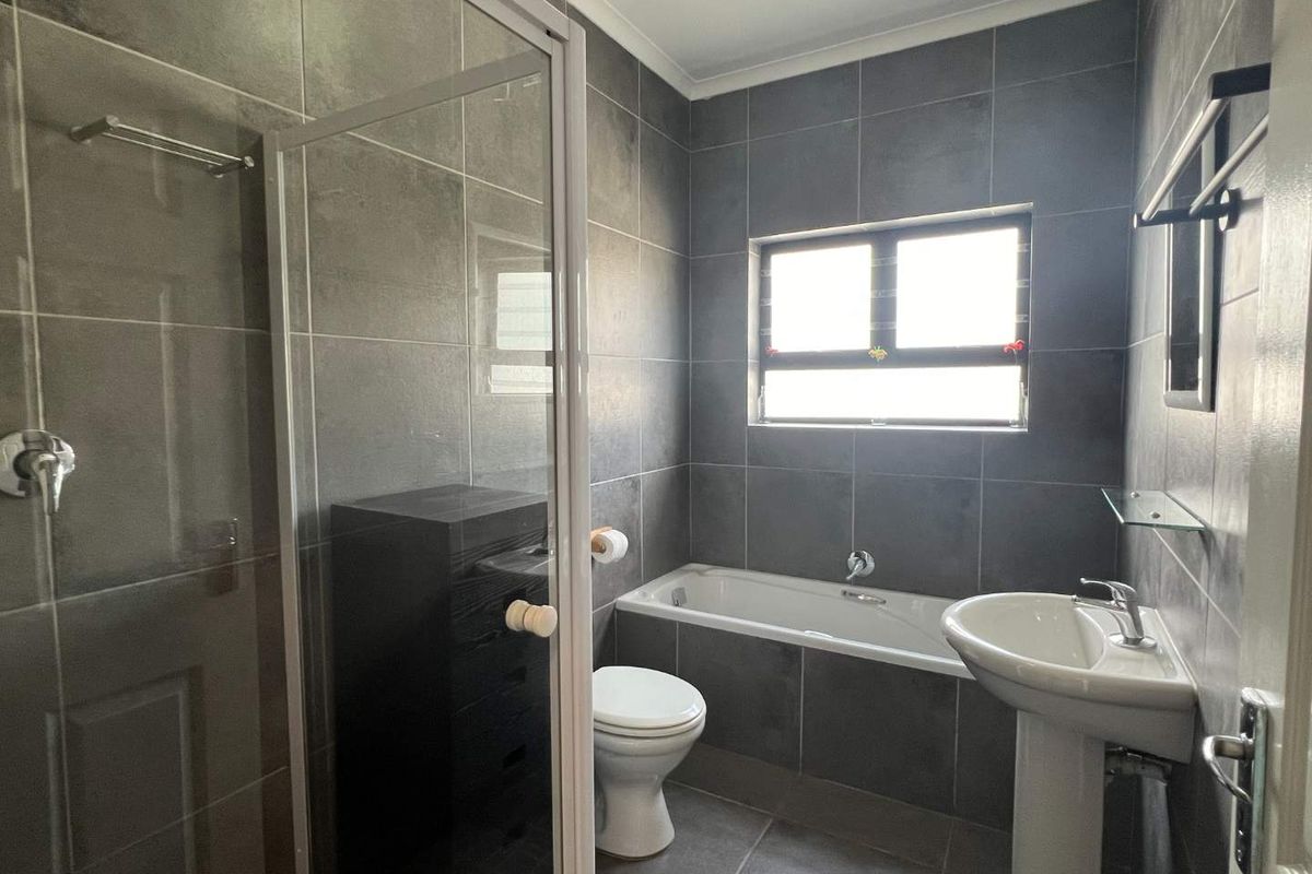 Modern bathroom featuring dark grey wall and floor tiles, a glass-enclosed shower, a built-in bathtub, and a white pedestal sink.