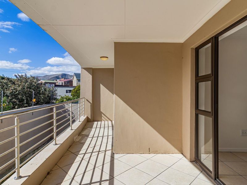 A clean, covered balcony featuring tiled flooring, a metal balustrade, and sliding glass door access to the interior.