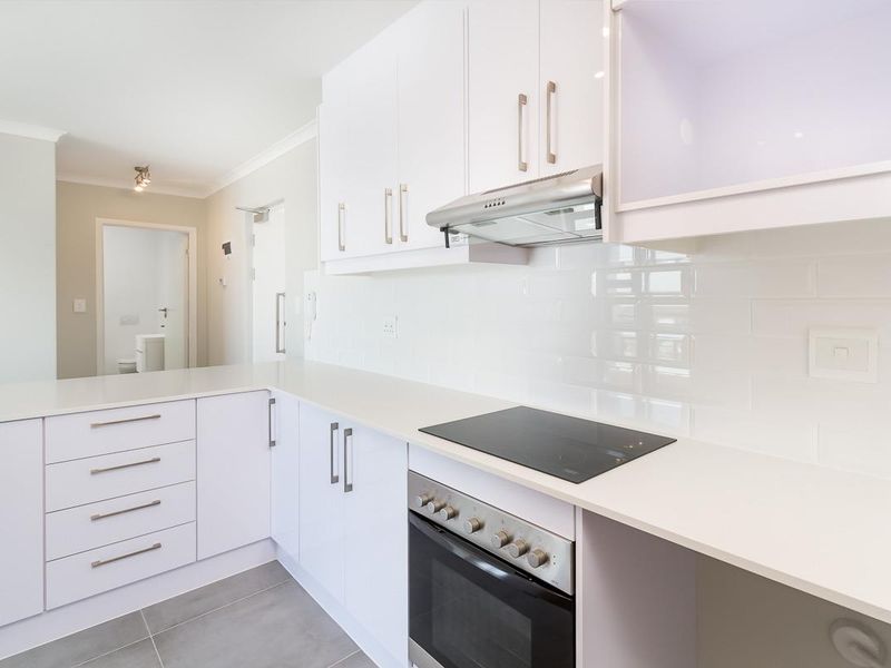 Modern kitchen featuring white cabinetry, stone countertops, subway tile backsplash, and integrated stainless steel appliances, including an electric cooktop and oven.