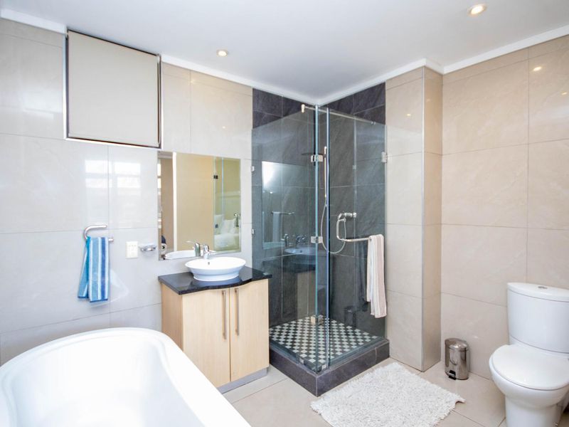 Modern bathroom featuring a glass-enclosed shower, vessel sink with vanity cabinet, and neutral wall tiling.