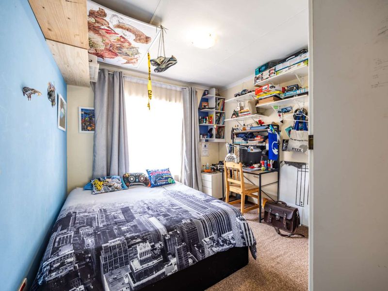 A compact bedroom featuring carpet flooring, built-in shelving units, and a window with curtains, providing a functional living space.