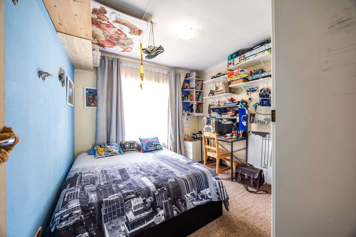 A compact bedroom featuring carpet flooring, built-in shelving units, and a window with curtains, providing a functional living space.
