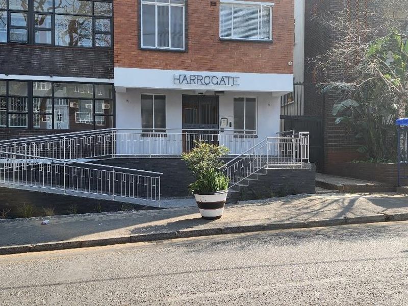 Front entrance of the Harrogate apartment building featuring a brick facade, accessible metal ramp, and secure entry point.