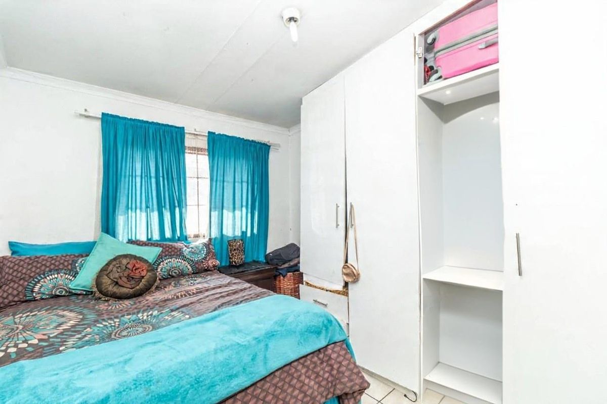 A bedroom featuring built-in white wardrobes and tiled flooring, requiring some cosmetic updates to the ceiling and wall finishes.