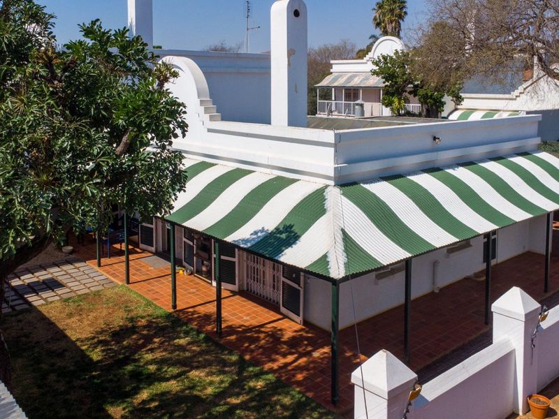 Rear view of the property featuring a covered patio with a striped corrugated metal awning, terracotta tiling, and a secure perimeter wall.