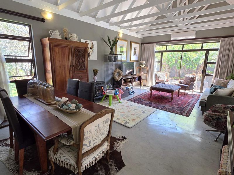 Spacious open-plan living and dining area featuring high vaulted ceilings with exposed rafters, polished concrete floors, and large glass doors opening to the garden.