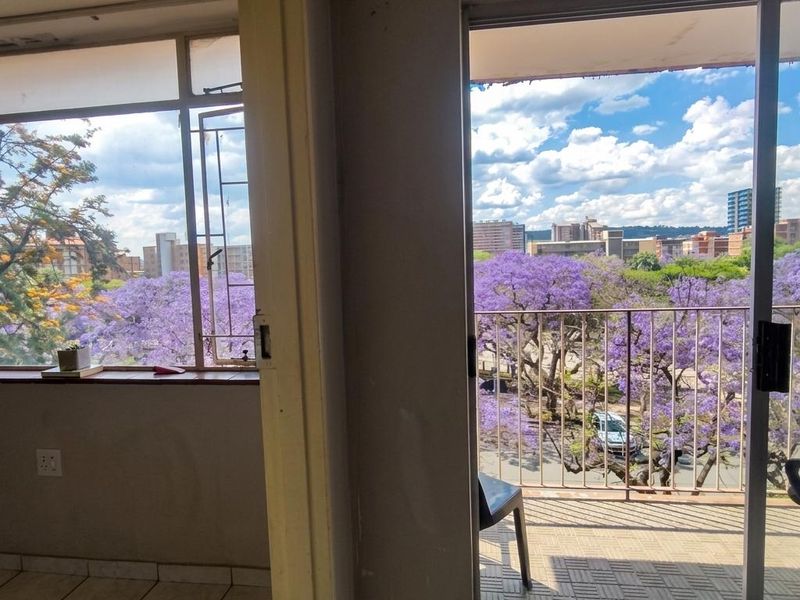 A view from an interior space onto a balcony featuring tiled flooring, a metal balustrade, and scenic urban views with flowering trees.