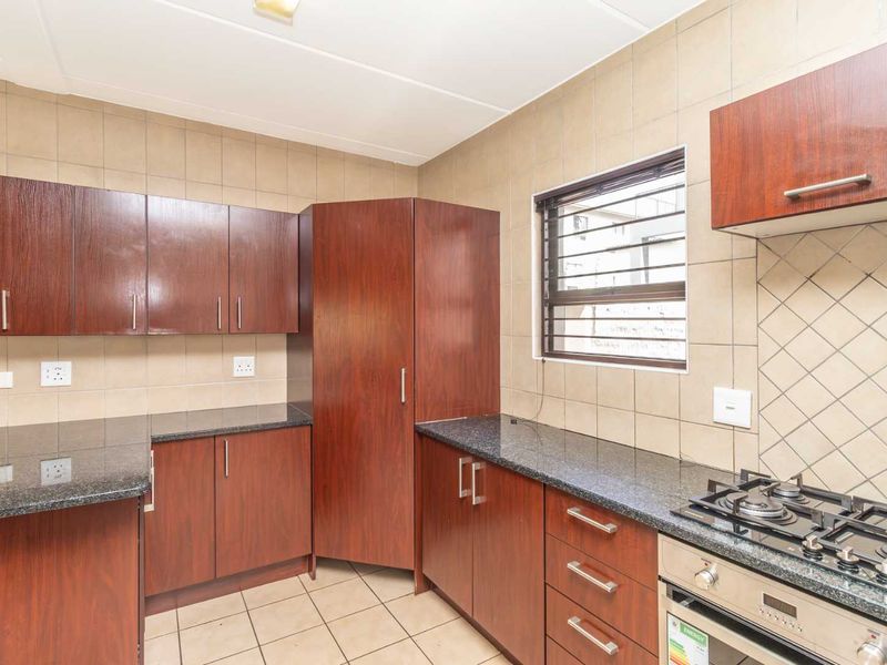 A functional kitchen featuring dark wood cabinetry, granite countertops, a built-in gas hob, and an oven, finished with neutral wall tiles and floor tiles.