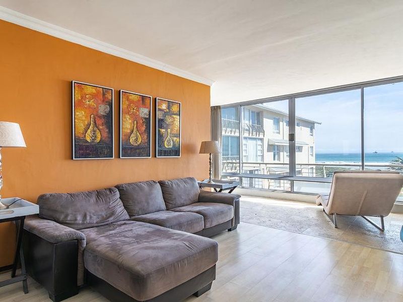 Spacious living area featuring large floor-to-ceiling windows with ocean views, combining laminate and stone flooring with a bright accent wall.