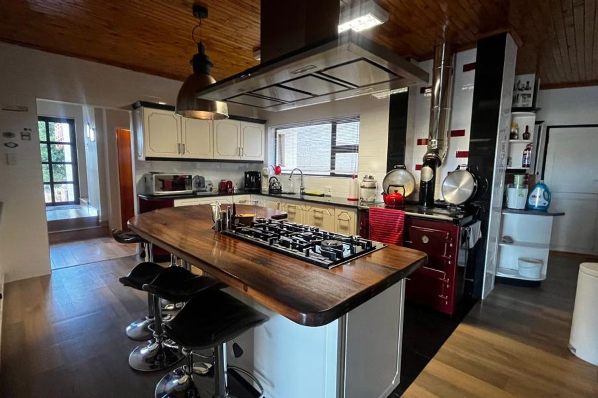 Spacious kitchen featuring a large central island with a built-in gas hob, wooden countertop, and a prominent red range cooker with an overhead extractor.