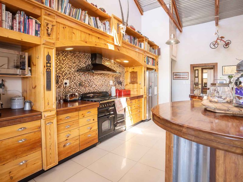 Rustic kitchen featuring extensive wooden cabinetry, mosaic tile backsplash, a large freestanding oven, and exposed timber roof beams with a corrugated metal ceiling.