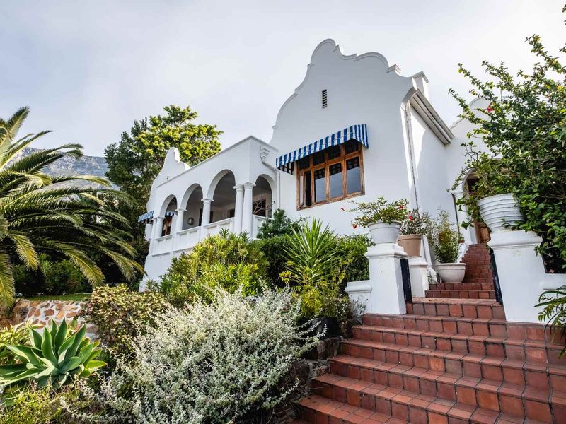 Charming Cape Dutch style home featuring a classic white facade, arched veranda, and a welcoming terracotta tiled staircase surrounded by lush garden landscaping.