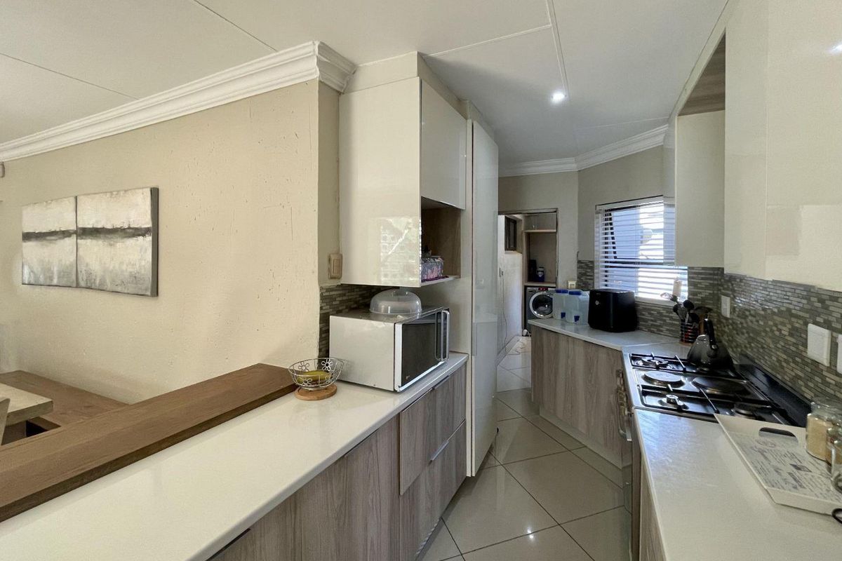 Modern kitchen featuring sleek built-in cabinetry, stone countertops, a gas hob, and a stylish mosaic tile backsplash with tiled flooring throughout.